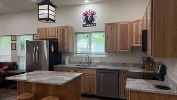 A modern kitchen with wooden cabinets, a stainless steel refrigerator, a sink, and a large island with stools.