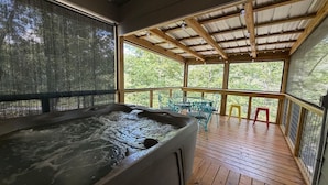 Un jacuzzi en un área exterior techada con piso de madera y barandillas metálicas.