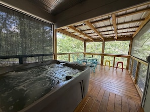 A hot tub in a covered outdoor area with wooden flooring and metal railings. - Brand-New Riverfront Escape with Kayak Access (Mentone)