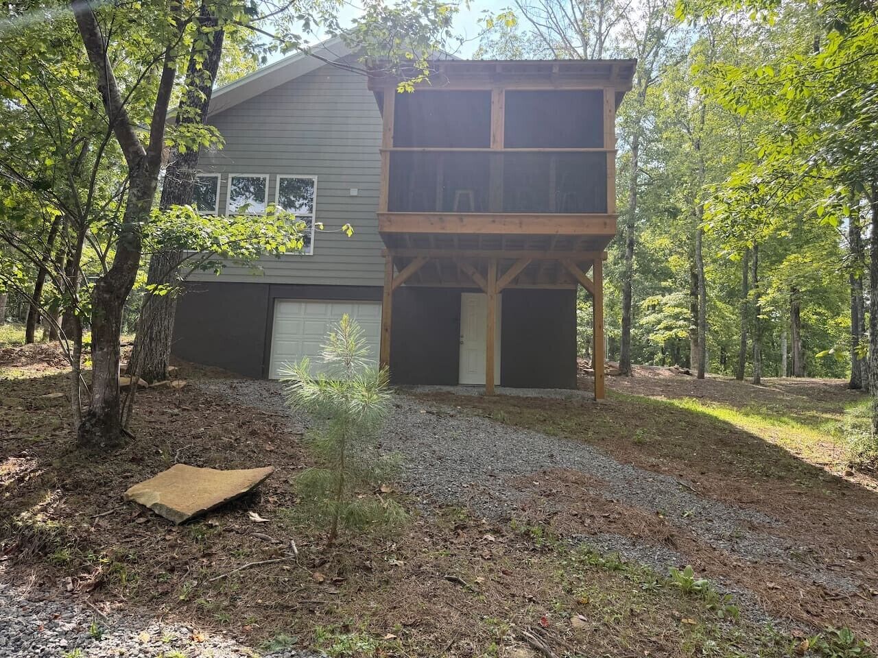 A two-story house with a garage, surrounded by trees and a gravel driveway.