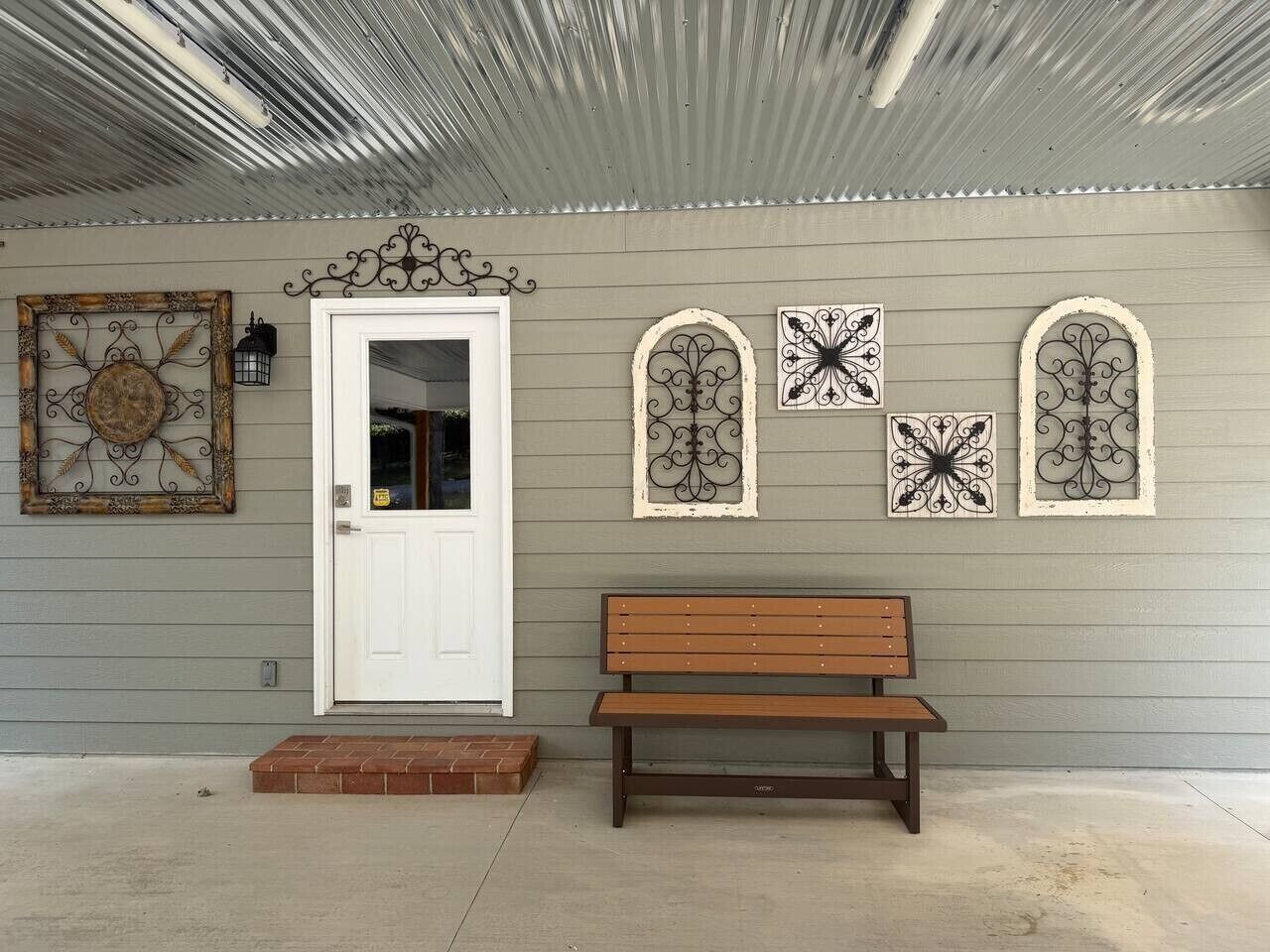Un banco de madera frente a una casa con puerta blanca y paneles de metal decorativos en la pared.