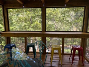 Un espacio de estar al aire libre cubierto con una mesa y sillas, rodeado por barandas de madera y ventanas amplias.