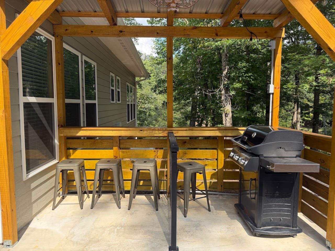 Een terras buiten met een barbecue en vier krukken.