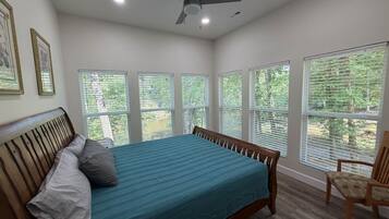 Un dormitorio con una cama, ventilador de techo y ventanas grandes.