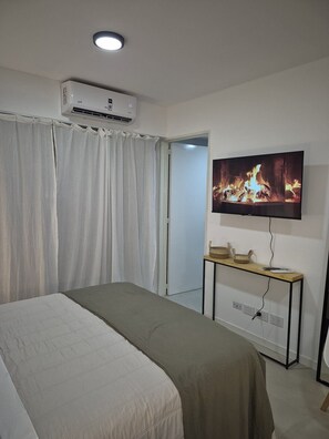 Ein Schlafzimmer mit einem Bett, einer Klimaanlage, einem Fernseher, der einen Kamin zeigt, und einem Nachttisch mit einem Korb.