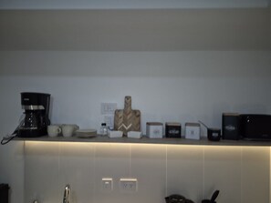Eine Küchenarbeitsplatte mit Kaffeemaschine, Tassen, Schneidebrett aus Holz und verschiedenen Behältern.