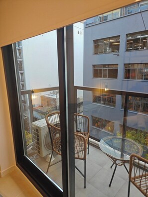 Ein Balkon mit Korbstühlen und einem Glastisch, mit Blick auf ein Gebäude mit zahlreichen Fenstern.