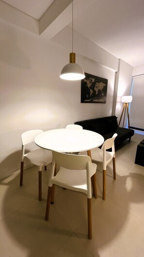 Un coin repas avec une table ronde et quatre chaises, un canapé noir, une carte du monde accrochée au mur et un lampadaire.