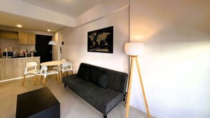 Ein modernes Wohnzimmer mit einer Couch, einem Esstisch mit Stühlen, einem schwarzen Couchtisch und einer Stehlampe.