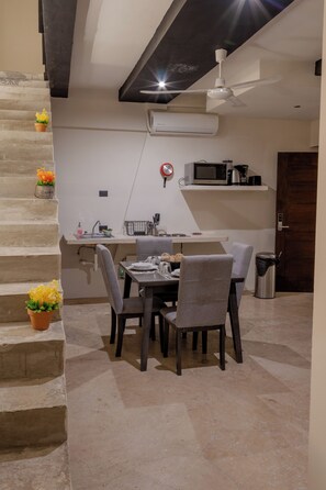 Un comedor con una mesa dispuesta para cuatro, sillas, ventilador de techo, equipo de aire acondicionado y un microondas en un estante.