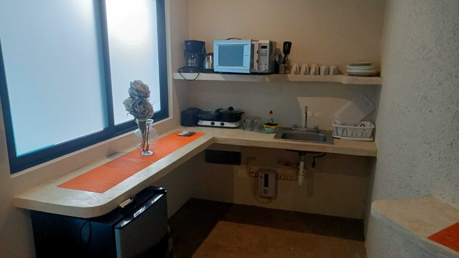 Una cocina compacta con microondas, cafetera y un lavamanos pequeño.