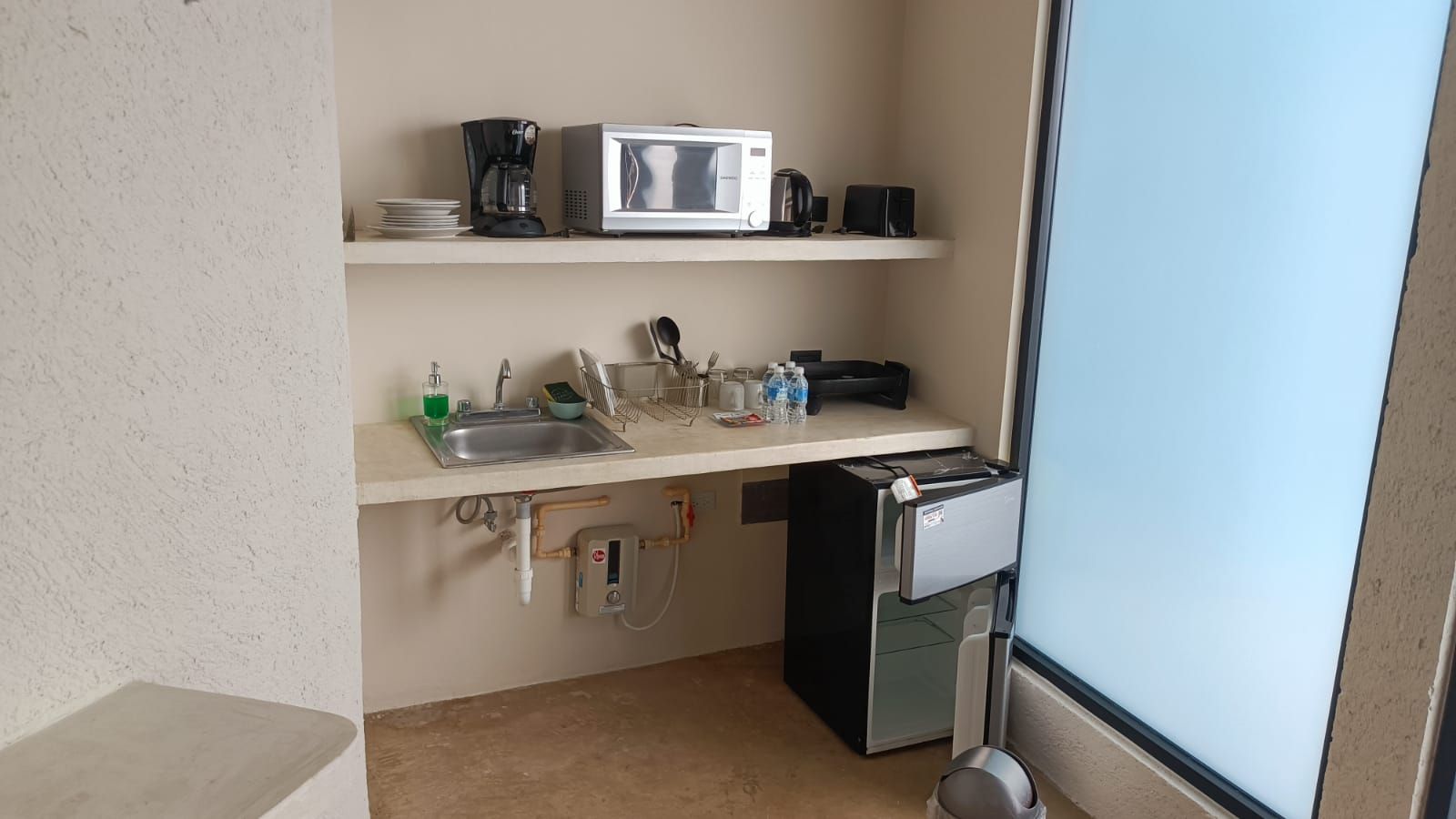 Una kitchenette compacta con microondas, cafetera y refrigerador pequeño.