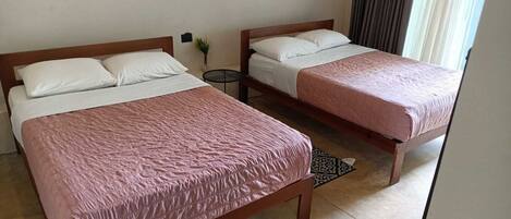 Two single beds with wooden frames and white bedding, a small round table, and a patterned rug on a tiled floor.