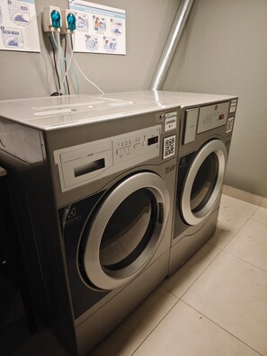 Eine Waschmaschine mit Frontlader, einem Bedienfeld, einem QR-Code und einer an der Wand befestigten Bedienungsanleitung.