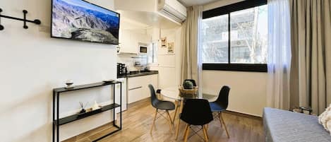A compact living space with a kitchenette, a dining area with a table and chairs, a bed, and a large window with curtains.