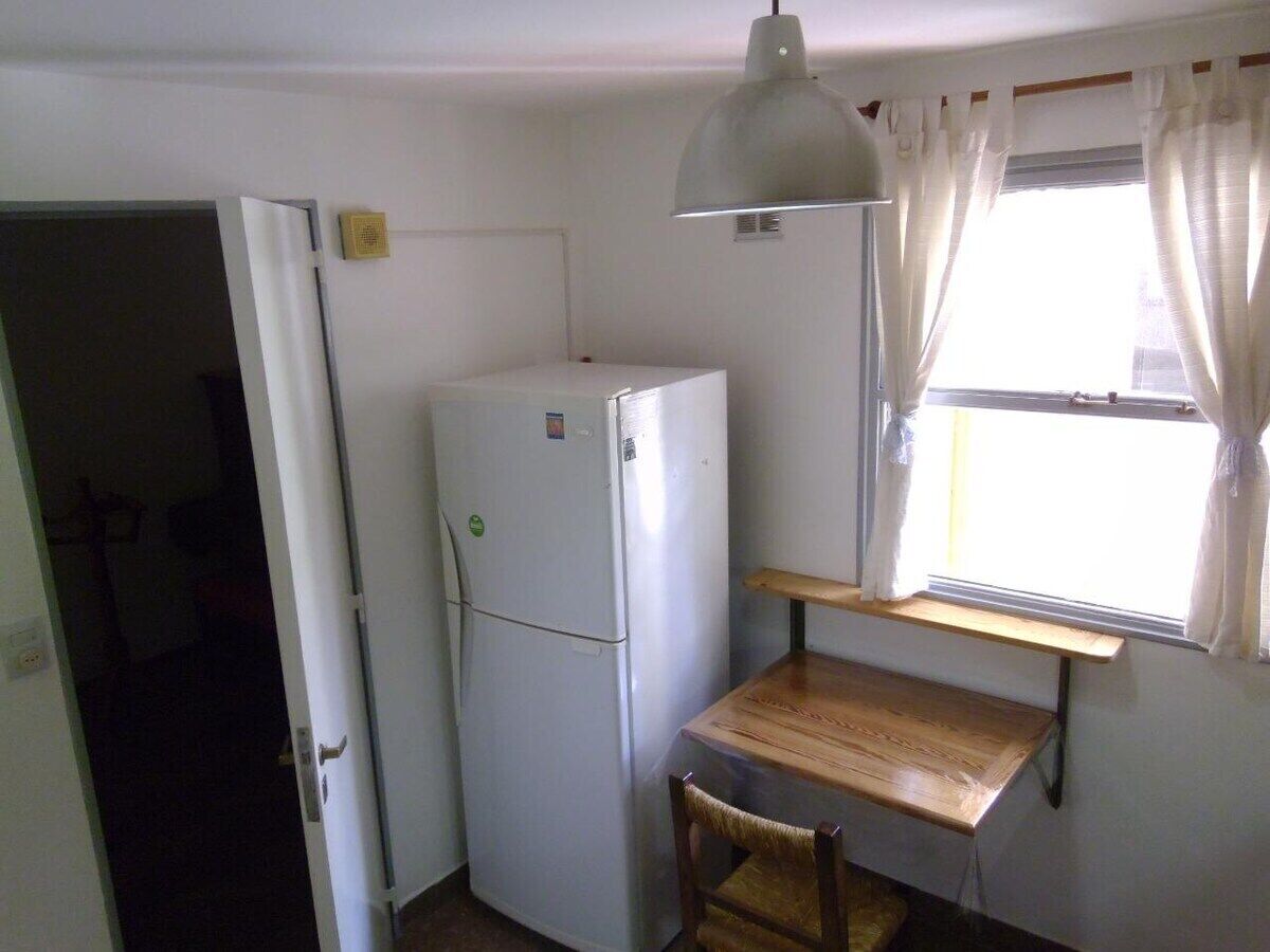 A compact kitchen with a white refrigerator, a wooden table, and a hanging light fixture.