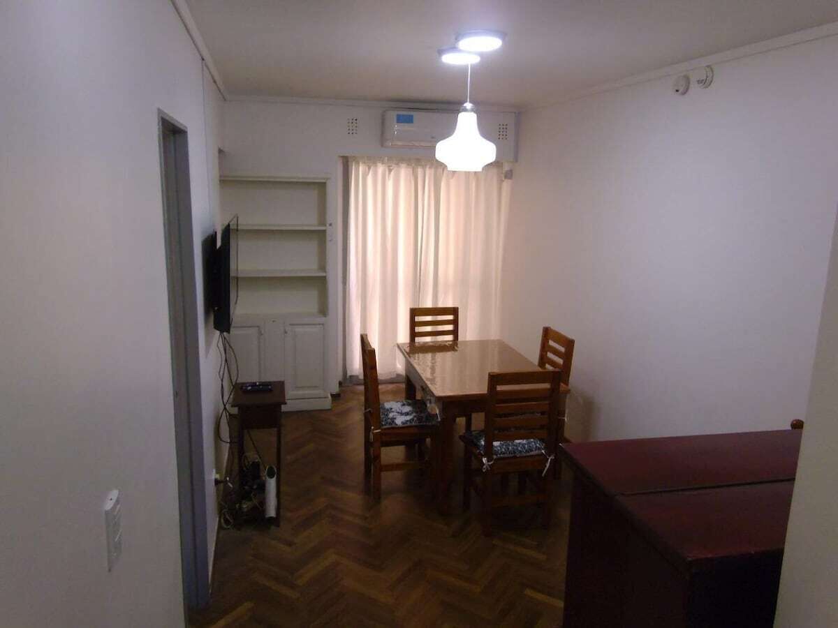 A dining area with a wooden table and chairs, a ceiling light fixture, and a window with curtains.