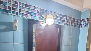 Casa de banho com azulejos azuis, uma pia branca, um espelho e um dispensador de sabonete.