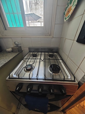 A kitchen with a gas stove, a window, and a tiled backsplash. - Departamento en calle Guemes (Buenos Aires)