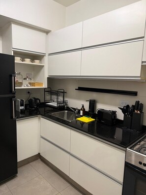 A modern kitchen with white cabinets, a black countertop, and stainless steel appliances including a refrigerator, a coffee maker, and a toaster. - Elegant & Spacious Apartment in Downtown BA (Buenos Aires)
