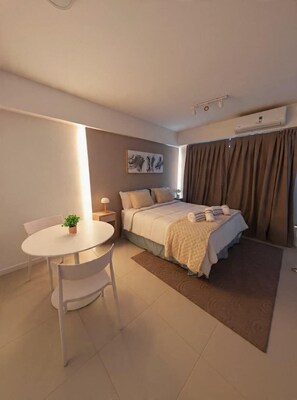 Un dormitorio con cama, mesita de noche, lámpara y una pequeña mesa con una planta.