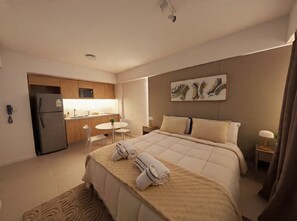 Ein modernes Hotelzimmer mit einem Bett, einer kleinen Küchenzeile, einem Essbereich und einem Badezimmer.