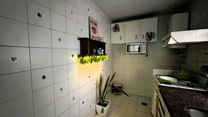 A kitchen with white tiled walls, a microwave, a stove, and a potted plant. - Jungle Chic in Palermo · Vibrant & Unique (Buenos Aires)