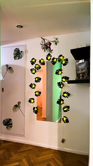 A room with a mirror reflecting a green wall, a wooden floor, and a shelf with a book and a DVD. - Jungle Chic in Palermo · Vibrant & Unique (Buenos Aires)