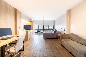 Ein modernes Zimmer mit Schreibtisch, Computer, Stuhl, Bett und Schlafsofa.
