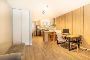 Ein kompakter Wohnbereich mit Küchenzeile, einer Essecke mit Tisch und Stühlen sowie einem separaten Arbeitsbereich mit Schreibtisch und Computer.