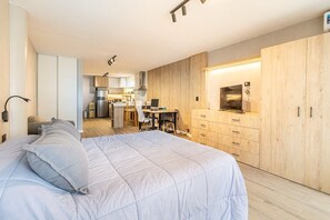 Ein modernes Schlafzimmer mit einem großen Bett, einem Schreibtisch und einer kleinen Küche im Hintergrund.