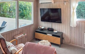 A cozy room with a flat-screen TV mounted on the wall, a wooden cabinet below, and a window with a view of greenery. - Pet friendly home in Ulfborg with WiFi (Ulfborg)