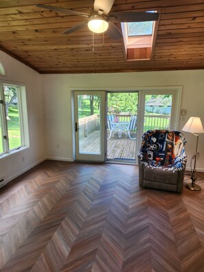 A room with a herringbone floor, a ceiling fan, a sliding glass door leading to an outdoor deck, and a sofa with a colorful blanket.