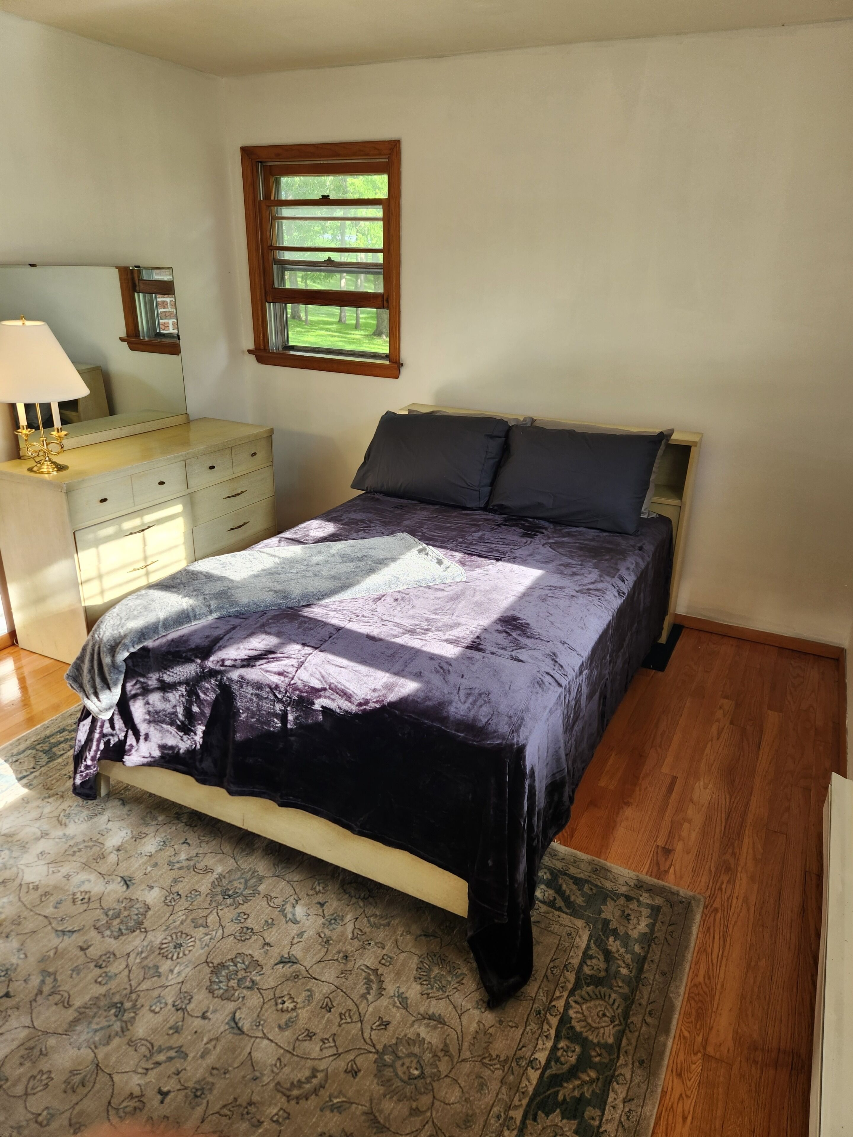 A bedroom with a bed, a dresser, a mirror, and a window.