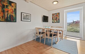 Een eetgedeelte met een tafel, stoelen, een televisietoestel en kunst aan de wanden.