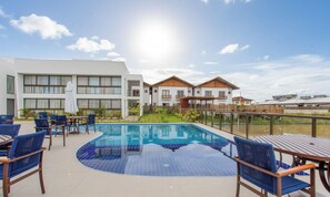 A swimming pool with blue tiles, surrounded by lounge chairs and tables, with buildings in the background. - Apt w/ 3 Suites in a Condo w/ a Pool Vll0010 (Maraú)