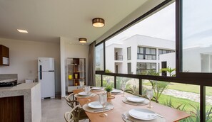 A modern kitchen with a dining area, large windows, and a view of a building. - Apt w/ 3 Suites in a Condo w/ a Pool Vll0010 (Maraú)