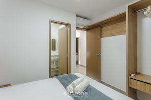 A hotel room with a bed, a wooden wardrobe, a bathroom with a mirror, and a ceiling air conditioner. - Apt With 3 Suites in a Condo With a Pool - Vll0009 (Maraú)
