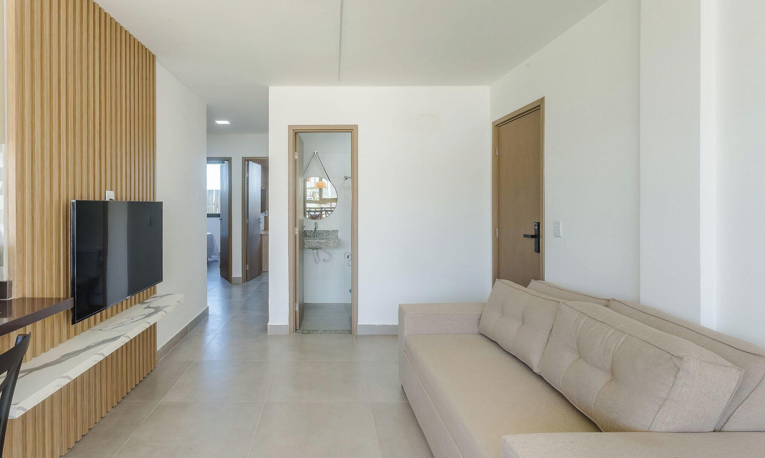A modern living room with a flat-screen TV, a beige sofa, and a wooden panel wall.