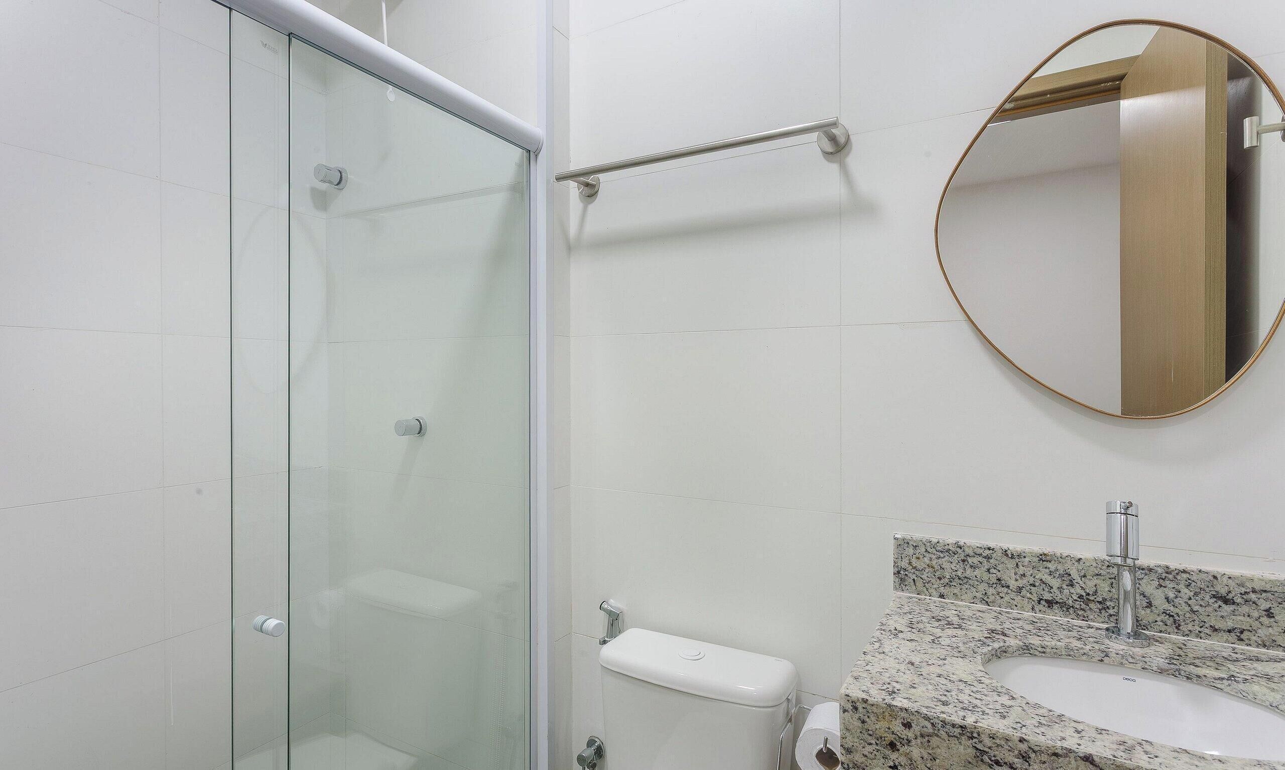 Ein Badezimmer mit Duschkabine aus Glas, einer Handstange, einer Toilette mit Papierhandtuchhalter und einer Waschtischplatte aus Granit.