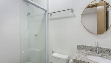 Ein Badezimmer mit Duschkabine aus Glas, einer Handstange, einer Toilette mit Papierhandtuchhalter und einer Waschtischplatte aus Granit.