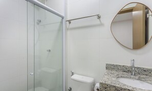 Un baño con cabina de ducha de vidrio, barra de apoyo, inodoro con dispensador de toallas de papel y encimera de granito con lavamanos.