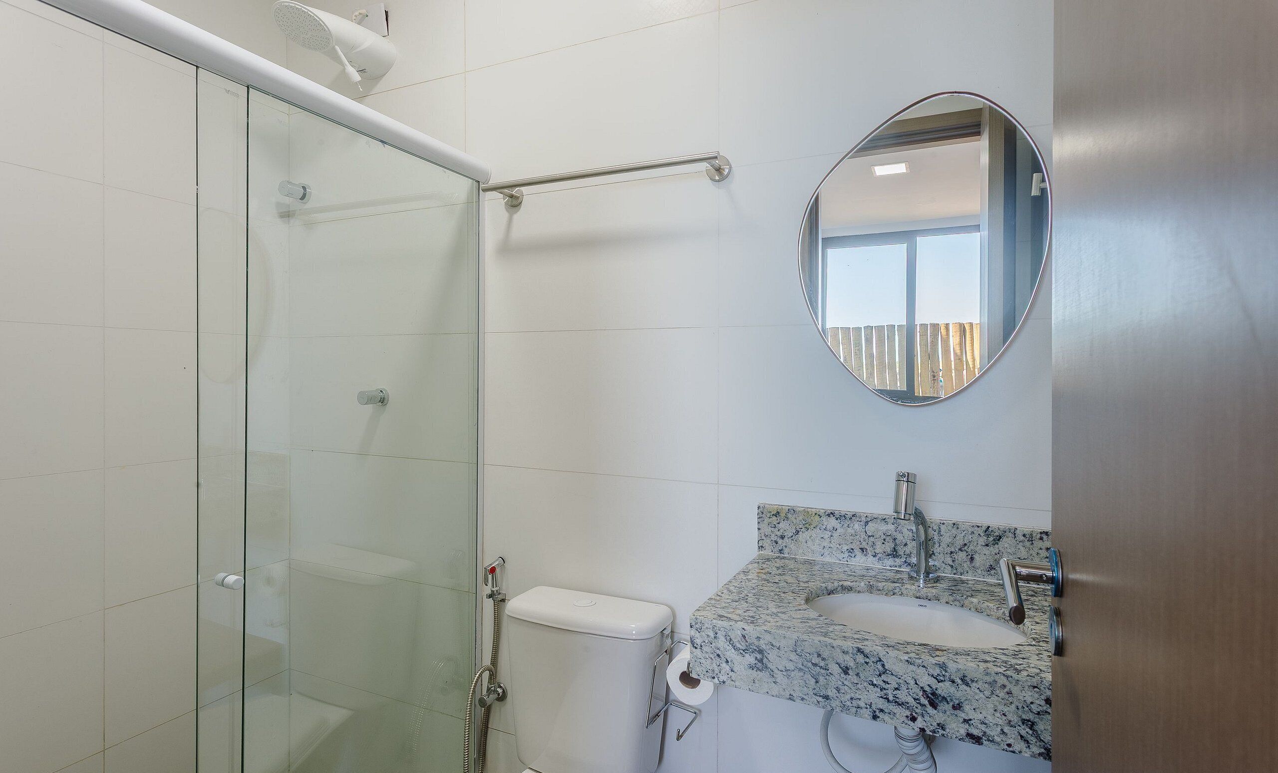 A bathroom with a glass shower enclosure, a toilet, a sink with a marble countertop, and a mirror.