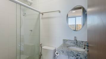 A bathroom with a glass shower enclosure, a toilet, a sink with a marble countertop, and a mirror.
