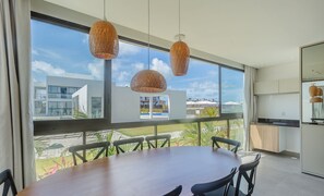 A modern dining area with a large table and chairs, large windows with a view of buildings, and hanging pendant lights. - Apt With 3 Suites in a Condo With a Pool - Vll0009 (Maraú)