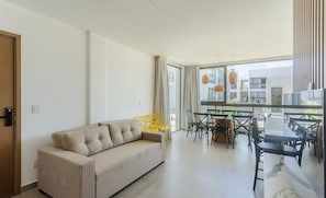 A modern living room with a sofa, dining area, and large windows. - Apt With 3 Suites in a Condo With a Pool - Vll0009 (Maraú)