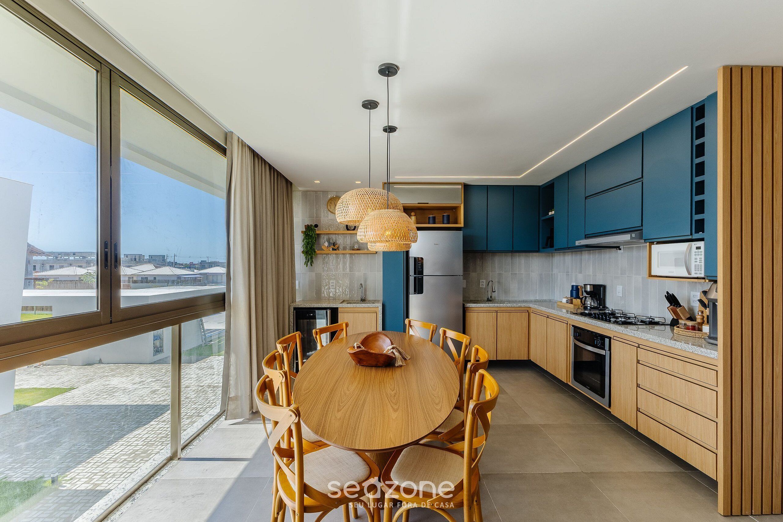 Una cocina moderna con una mesa redonda de madera, armarios azules y un amplio ventanal con vistas a la ciudad.