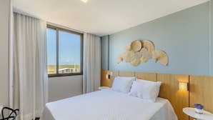 A hotel room with a large bed, a view through the window, and a decorative wall piece. - Apto Encantador Cerca del mar en Marau Vll0107 (Maraú)