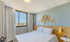 Quarto de hotel com uma cama grande, vista pela janela e um objeto decorativo na parede.