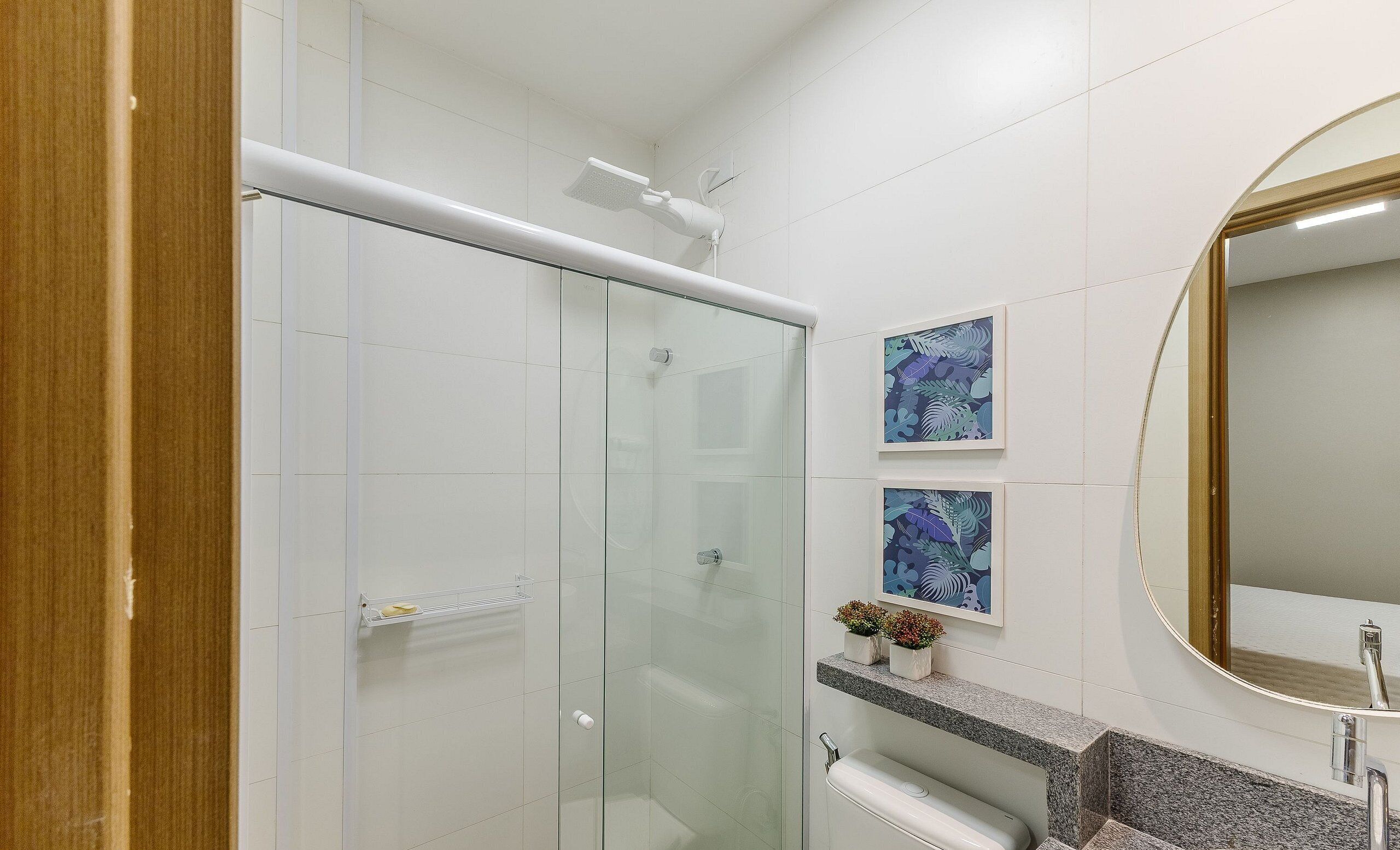 Un baño moderno con cabina de ducha de vidrio, encimera de granito, lavabo y dos obras de arte enmarcadas.
